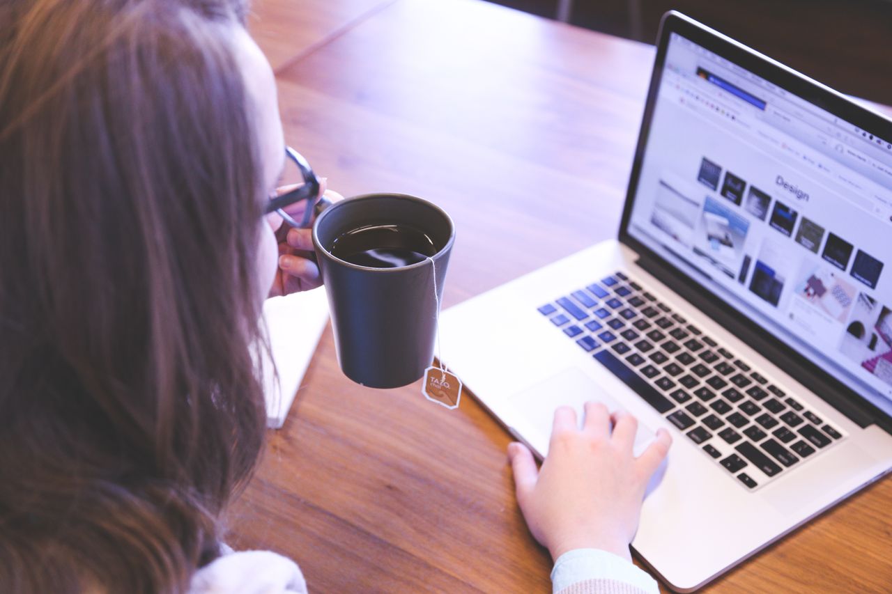 Services A woman enjoys coffee while browsing the web on a laptop at a home office desk.